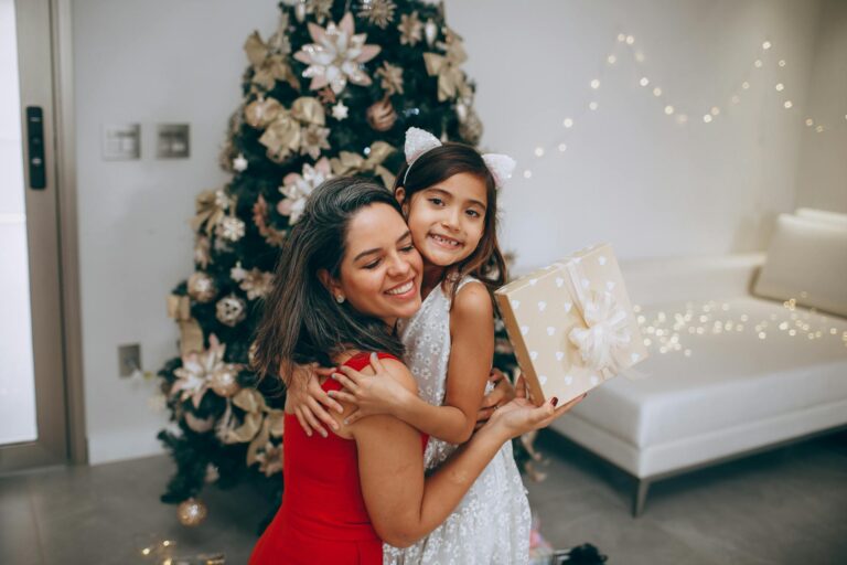 family fun Christmas singing activities, mother and daughter smiling and hugging with Christmas tree on the backdround