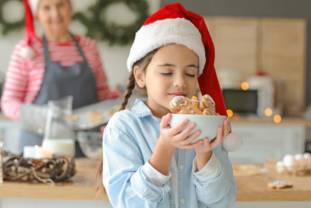 Family baking easy Christmas cookie recipe together and listening to Christmas playlist. Little girl is smelling freshly baked Christmas cookies. Grandma is smiling proudly while watching her granddaughter and making more Christmas cookies.