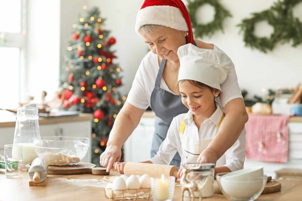 Family baking together easy Christmas cookie recipe, grandmother is helping little girl with rolling the dough